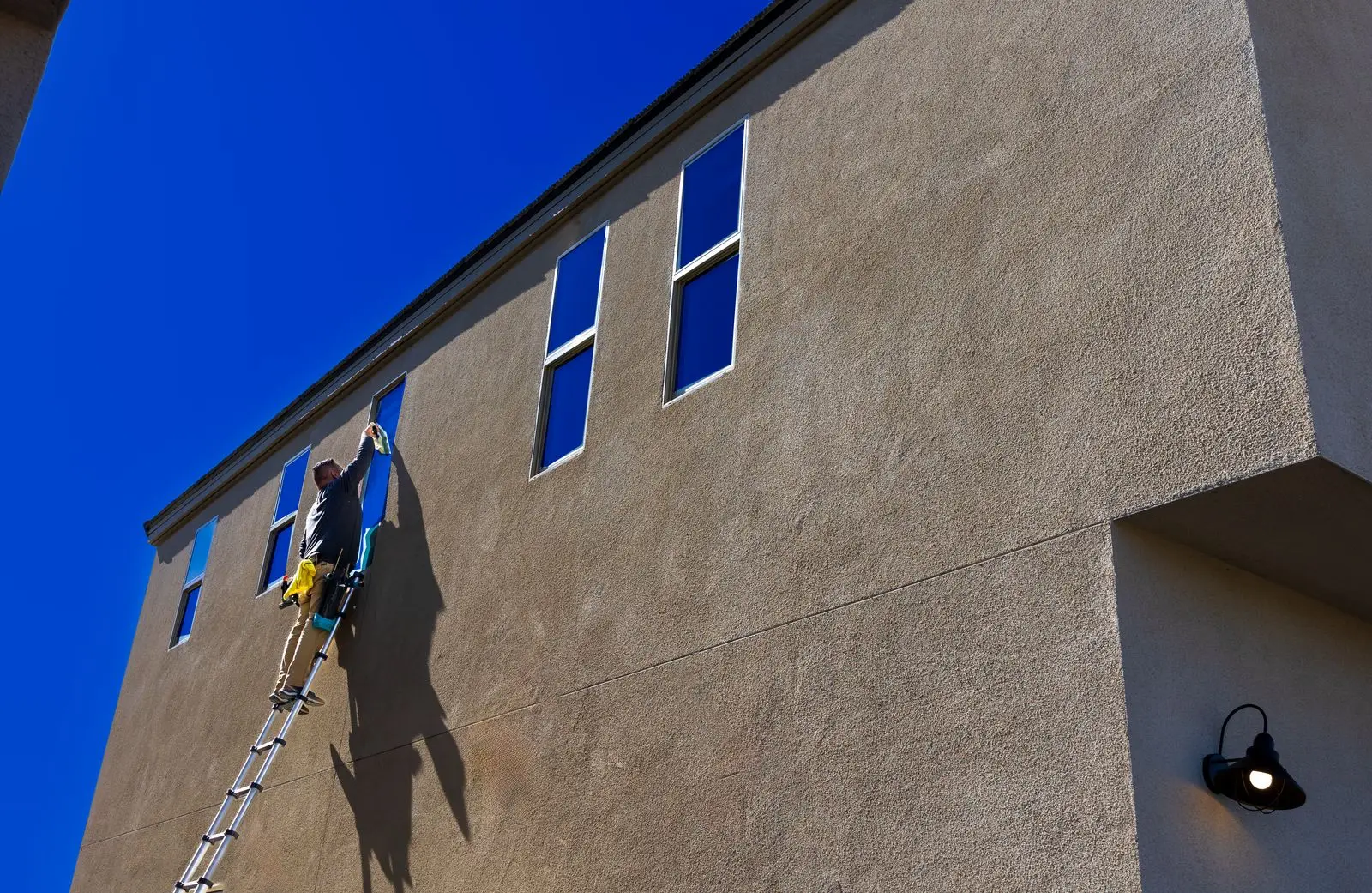 Glazenwasser op een hoge ladder reikt boven zijn hoofd om een raam in een hoge gevel te lappen